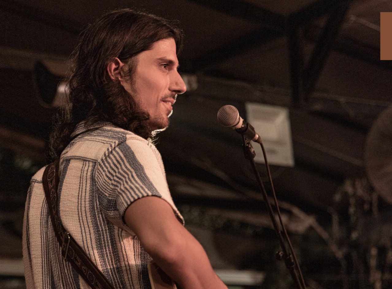 Itay Spiegel on stage at a microphone with a guitar strap over his shoulder