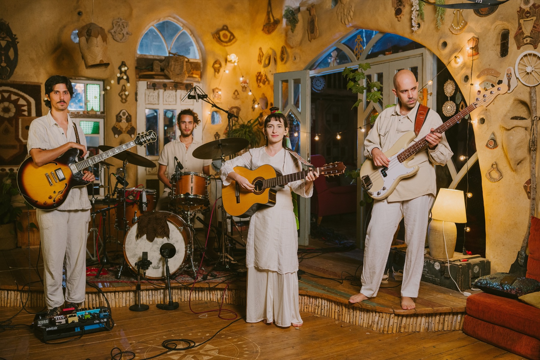 The band in white playing guitars, bass and drums in a colourful courtyard